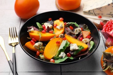 Photo of Delicious persimmon salad and fork on tiled surface