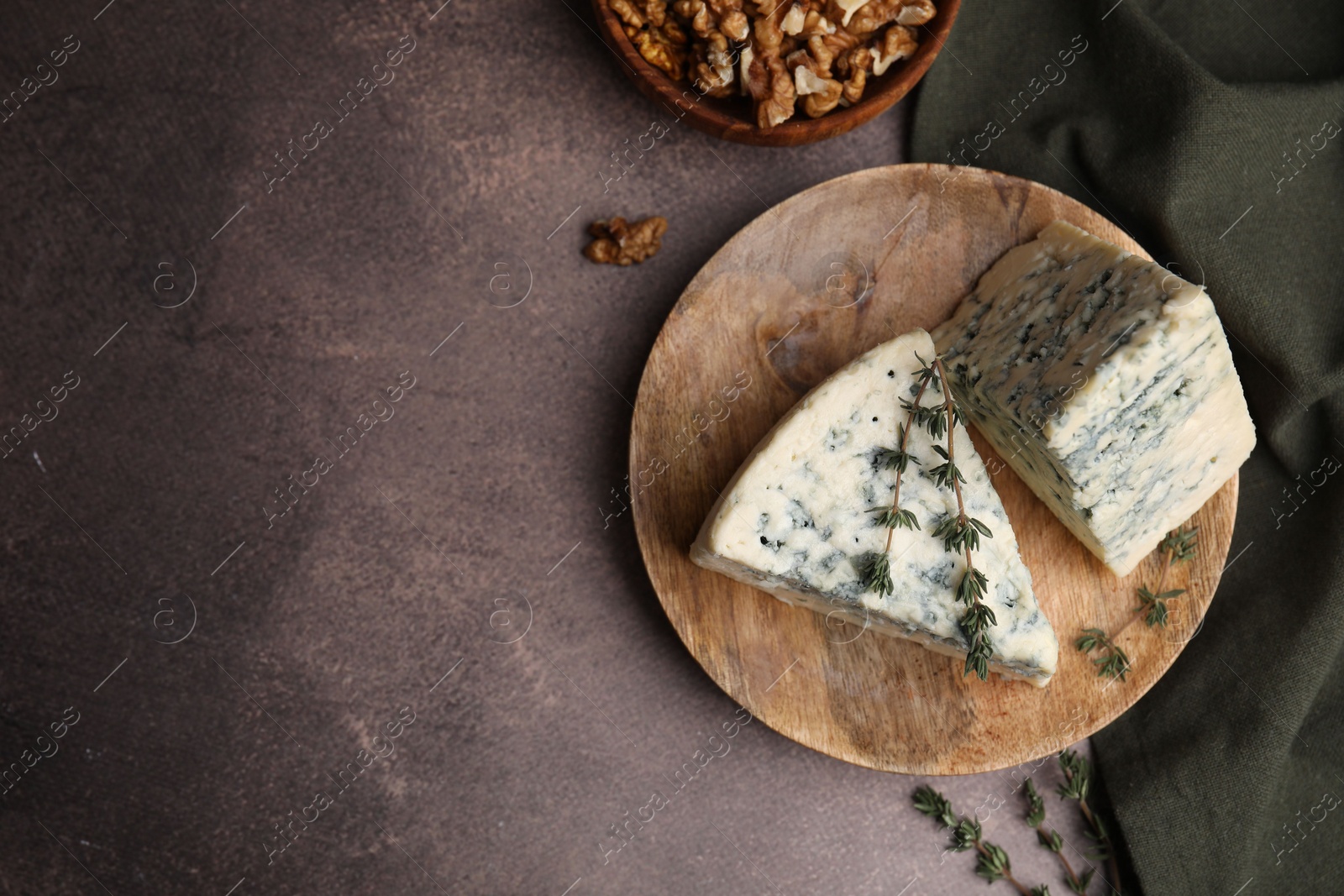 Photo of Tasty blue cheese with thyme and walnuts on brown table, flat lay. Space for text