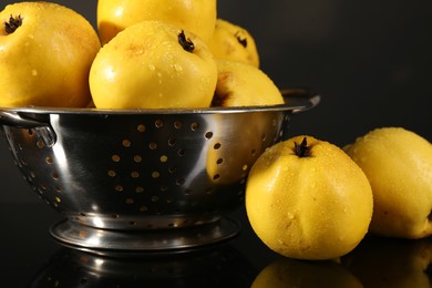 Tasty ripe quinces and metal colander on black mirror surface, closeup
