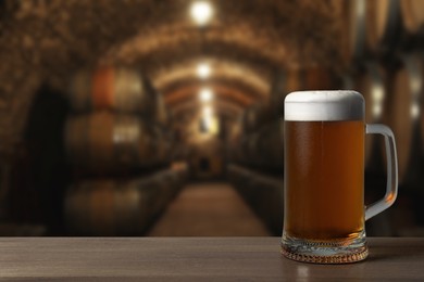 Image of Mug with fresh beer on wooden table in cellar, space for text