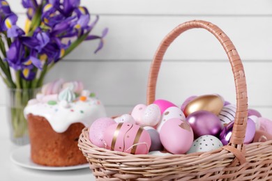 Wicker basket with festively decorated Easter eggs on white table, closeup