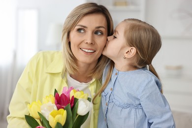 Photo of Little daughter kissing and congratulating her mom with Mother`s Day at home. Woman holding bouquet of beautiful tulips