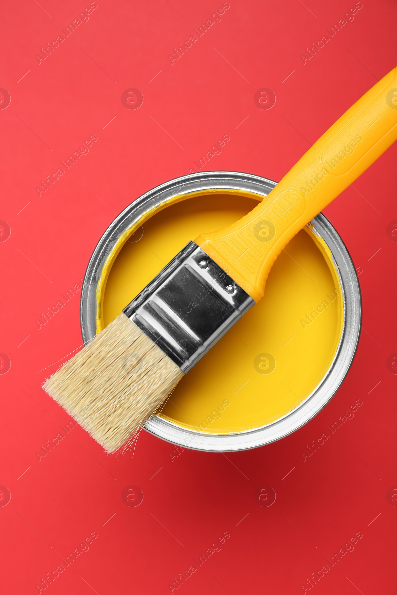 Photo of Can of yellow paint with brush on red background, top view