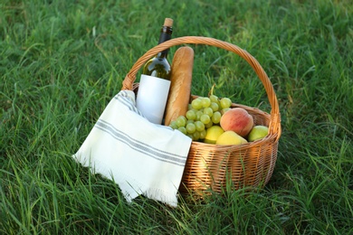 Photo of Picnic basket with snacks and bottle of wine on green grass in park