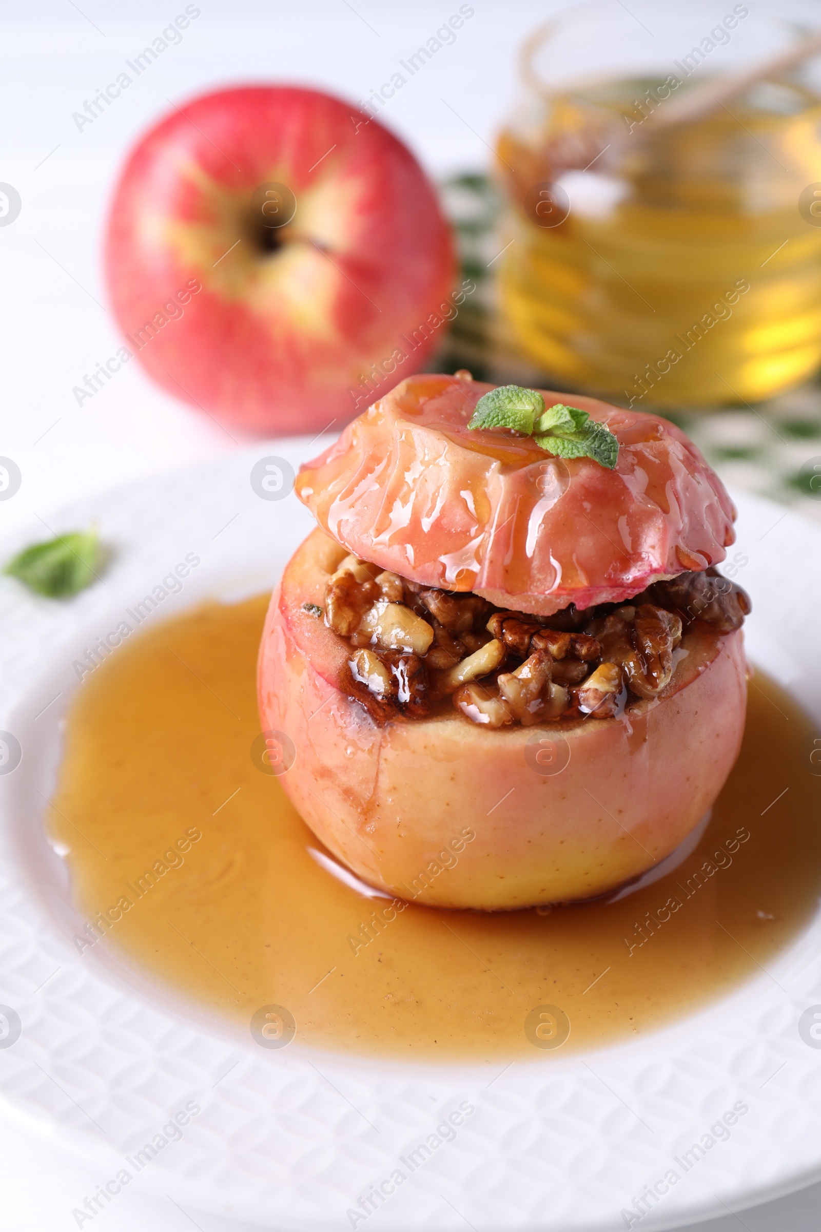 Photo of Tasty baked apple with nuts, honey and mint on white table, closeup