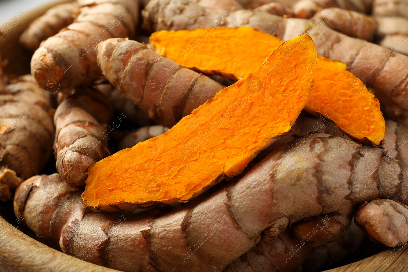 Photo of Whole and cut turmeric roots in bowl, closeup