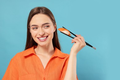 Photo of Happy young woman holding sushi with chopsticks on light blue background