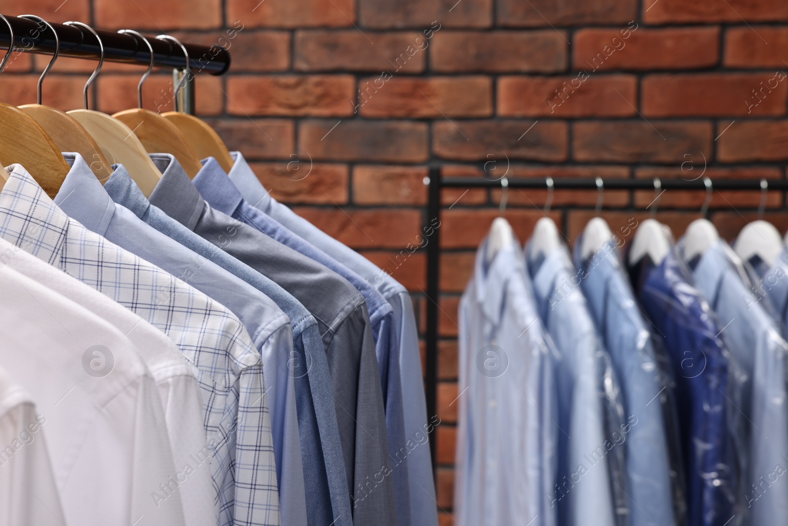 Photo of Dry-cleaning service. Many different clothes hanging on rack against brick wall, closeup