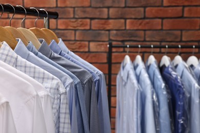 Dry-cleaning service. Many different clothes hanging on rack against brick wall, closeup