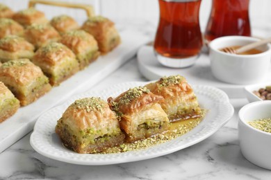Photo of Delicious fresh baklava with chopped nuts and honey on white marble table, closeup. Eastern sweets