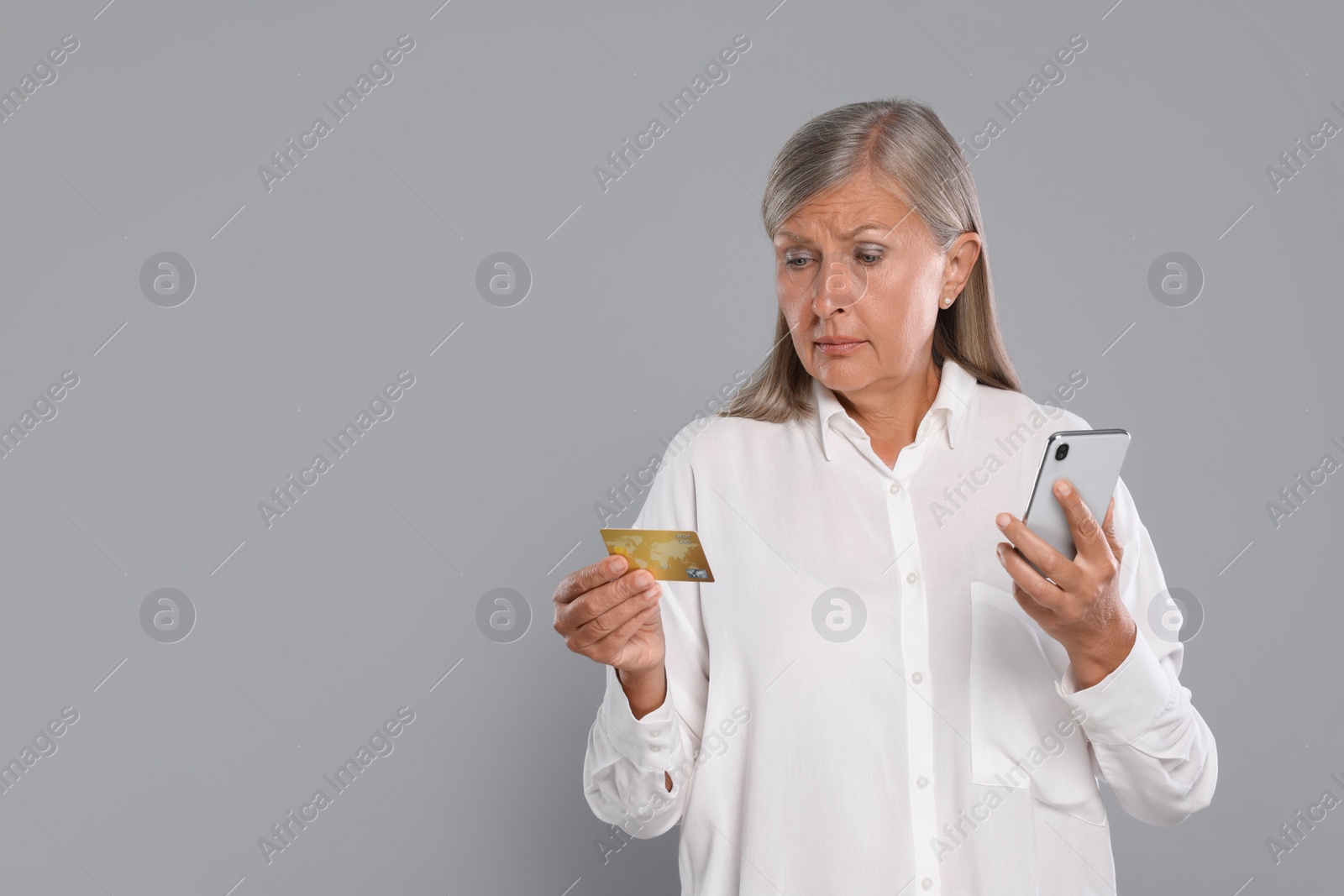 Photo of Worried woman with credit card and smartphone on light grey background, space for text. Be careful - fraud