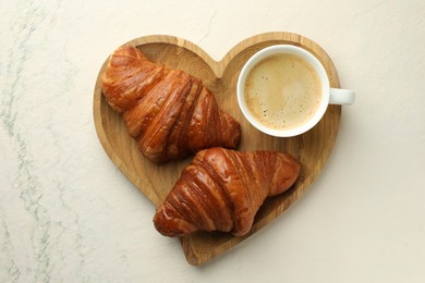 Tasty croissants served with cup of hot drink on light textured table, top view