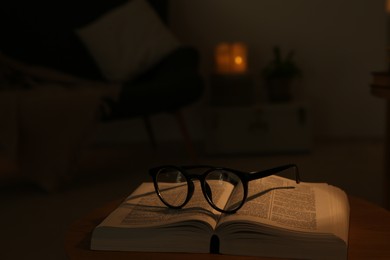 Photo of Book and glasses on wooden coffee table indoors at night
