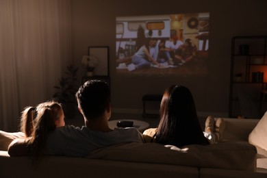 Photo of Family watching movie on sofa at night, back view