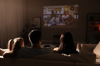 Family watching movie on sofa at night, back view