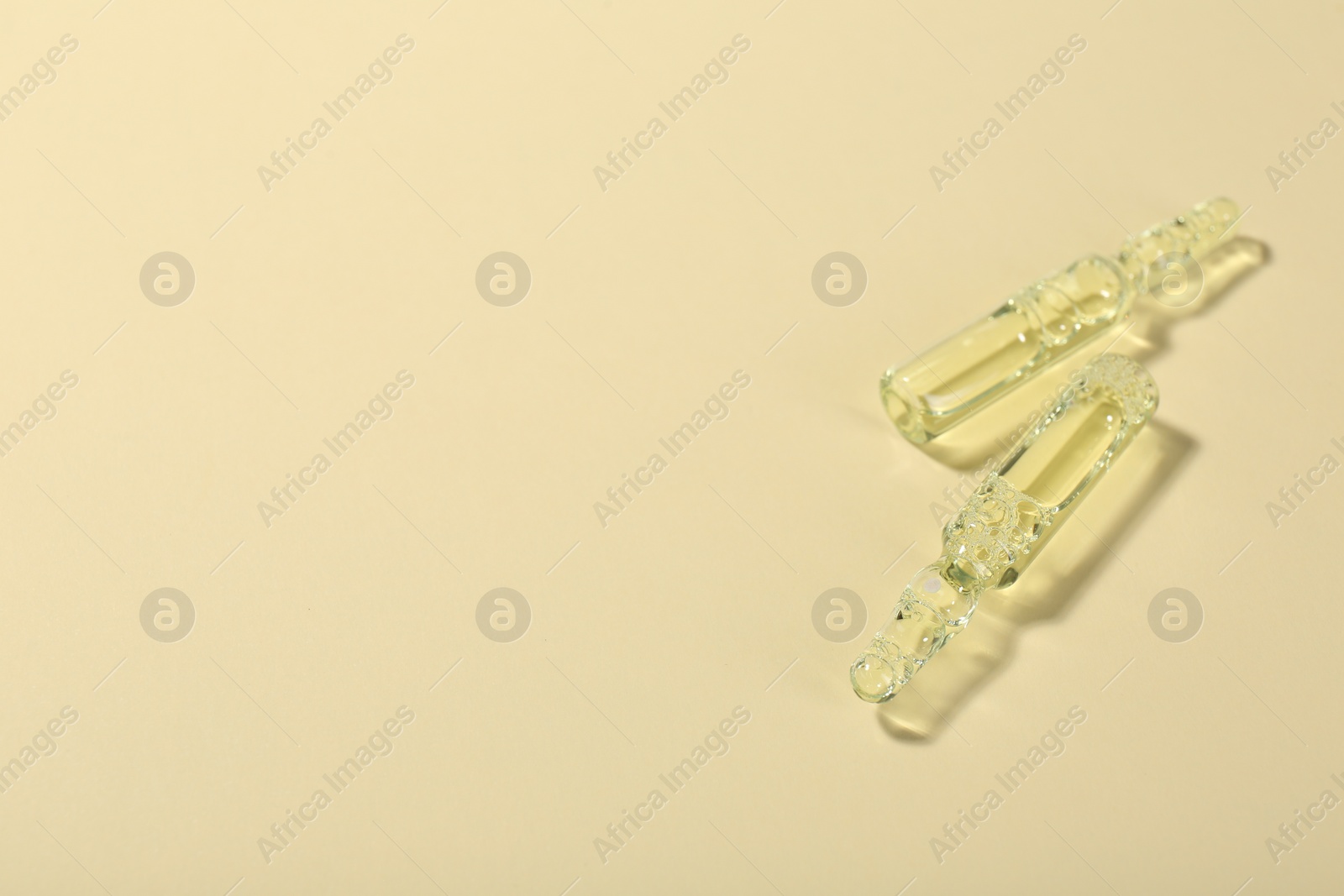 Photo of Glass ampoules with liquid on beige background. Space for text