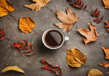 Cup of hot drink and autumn leaves on grey table, flat lay. Cozy atmosphere