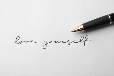 Photo of Written words LOVE YOURSELF and pen on white background, top view