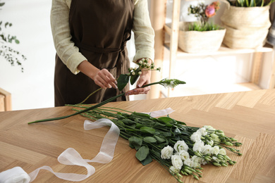 Florist making beautiful bouquet at table in workshop, closeup