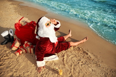 Santa Claus with cocktail and bag of presents relaxing on beach. Christmas vacation