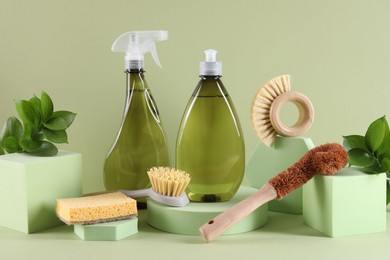 Bottles of cleaning product, sponge and brushes on light green background