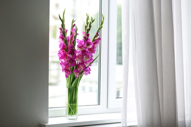 Photo of Vase with beautiful pink gladiolus flowers on windowsill, space for text