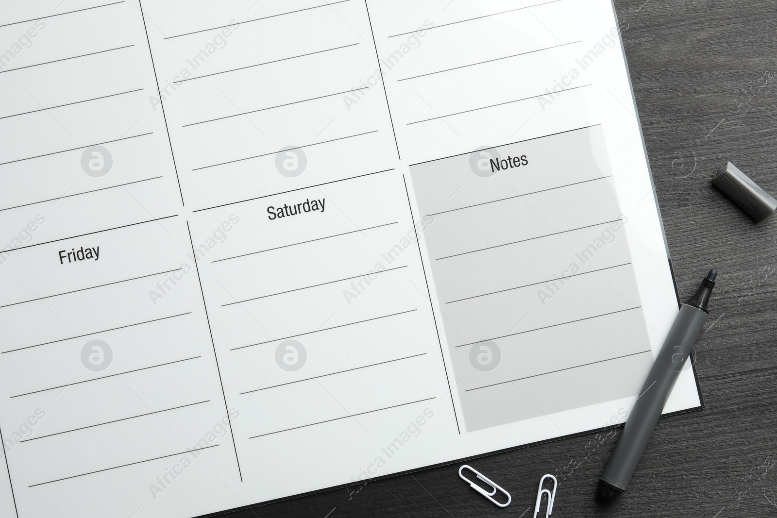 Photo of Timetable. Weekly planner, felt pen and paper clips on black wooden table, top view