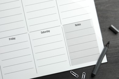 Photo of Timetable. Weekly planner, felt pen and paper clips on black wooden table, top view