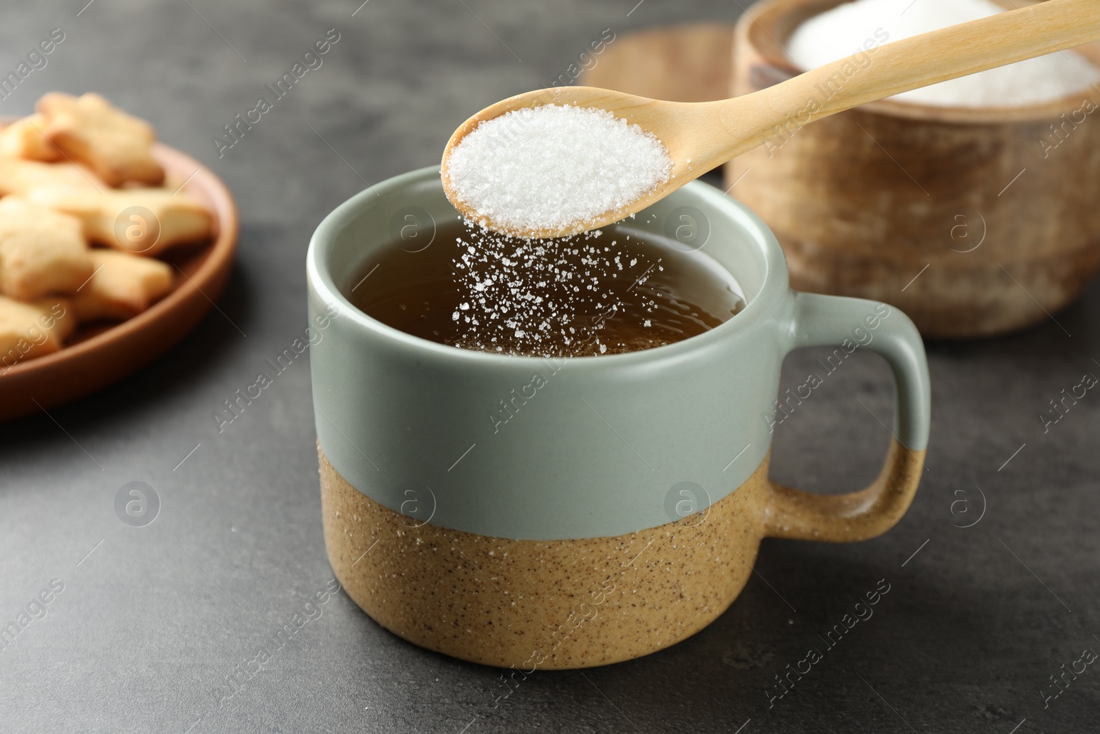 Photo of Adding sugar into aromatic tea at grey table, closeup
