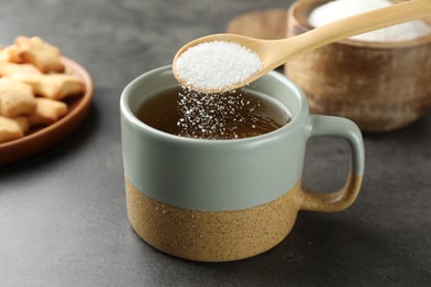 Adding sugar into aromatic tea at grey table, closeup