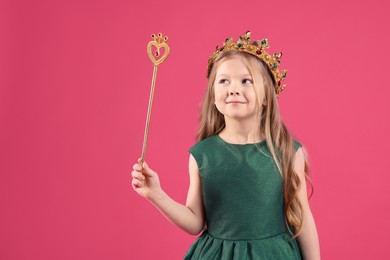 Photo of Cute girl in fairy dress and golden crown holding magic wand on pink background. Little princess