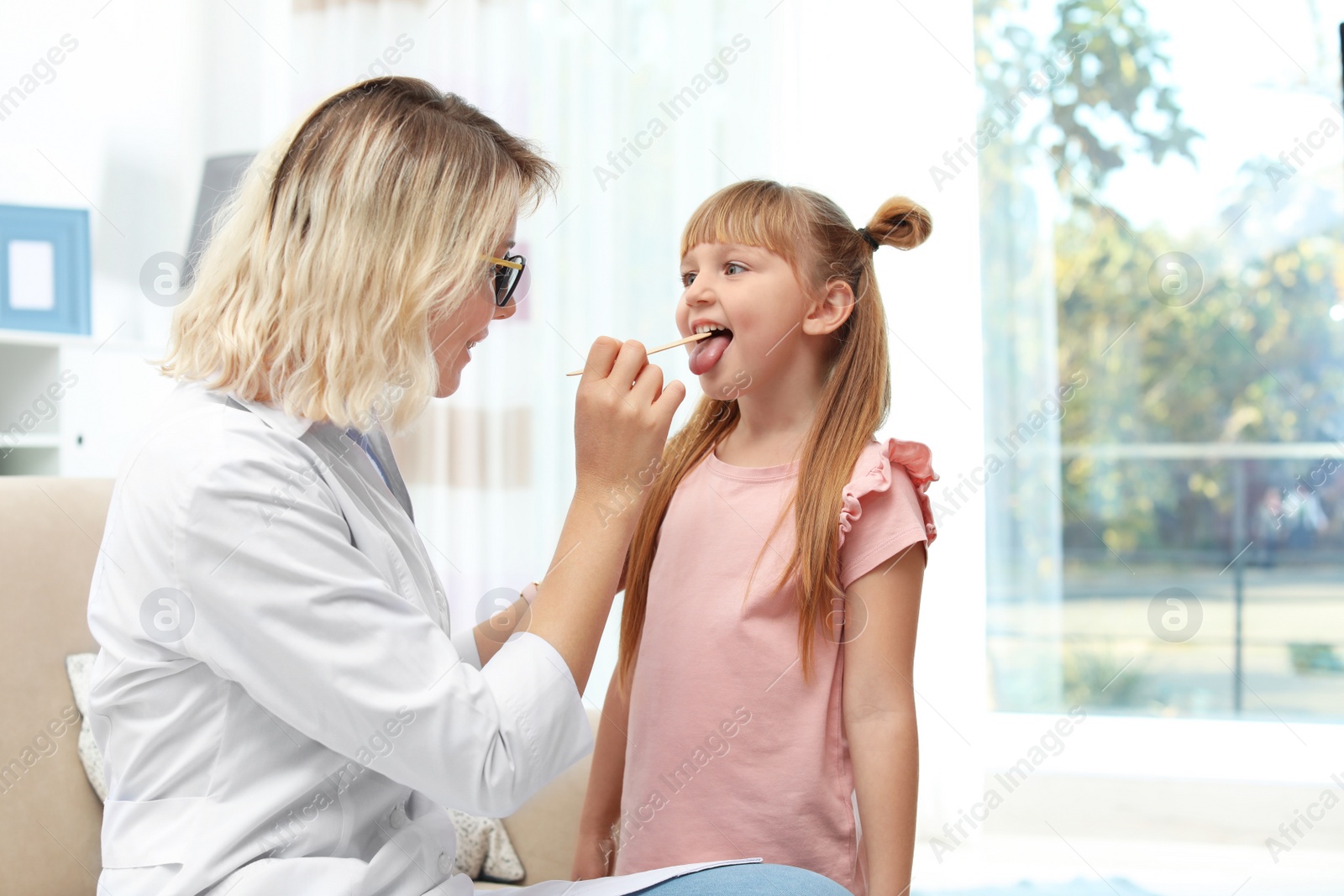 Photo of Children's doctor examining little girl's throat at home. Space for text