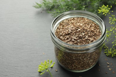 Photo of Dry seeds and fresh dill on black table, closeup. Space for text