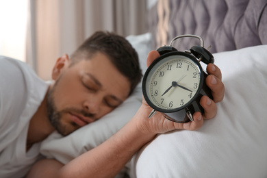 Man with alarm clock sleeping at home in morning, focus on hand