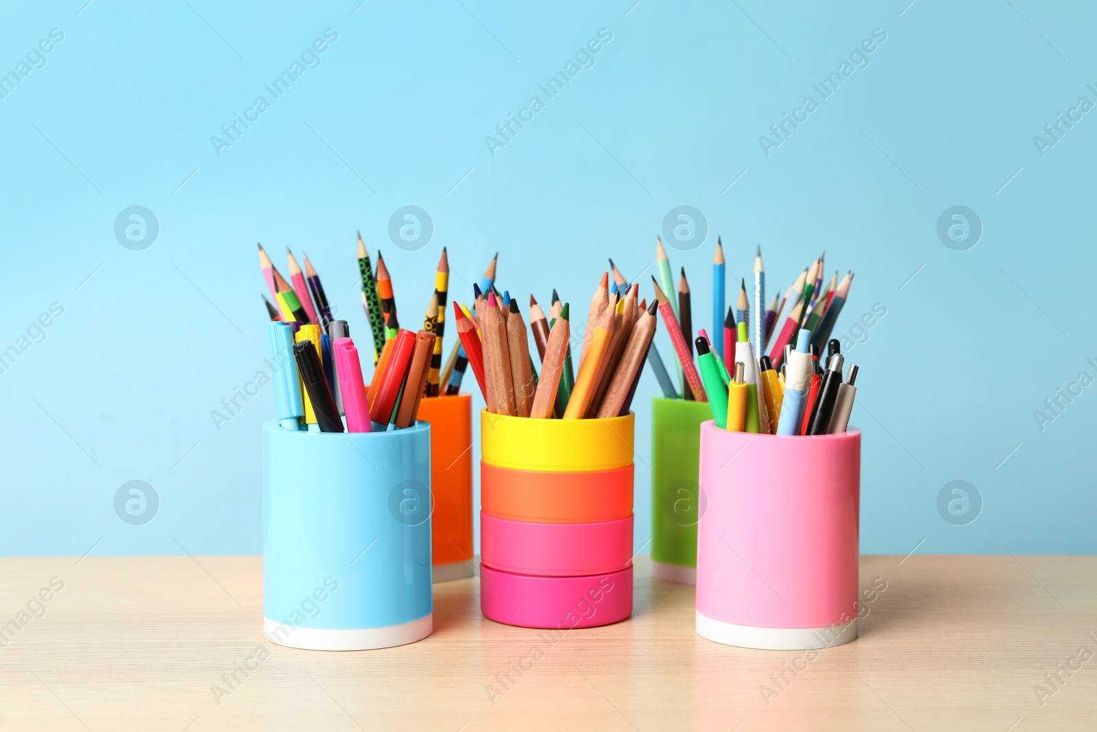 Photo of Holders with different school stationery on wooden table against light blue background. Back to school