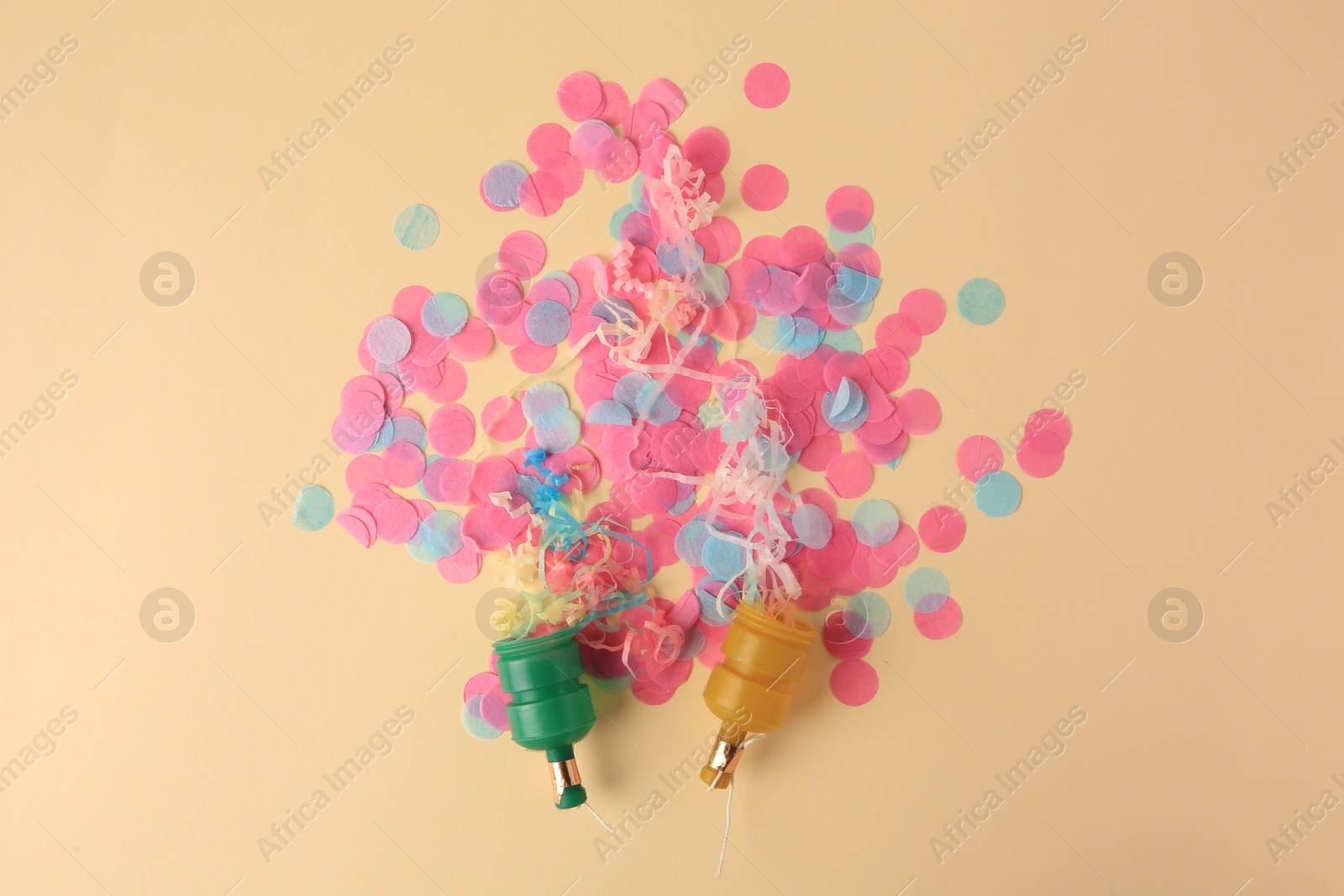 Photo of Colorful confetti and serpentine bursting out of party poppers on beige background, flat lay