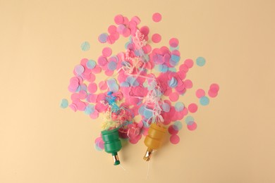 Photo of Colorful confetti and serpentine bursting out of party poppers on beige background, flat lay