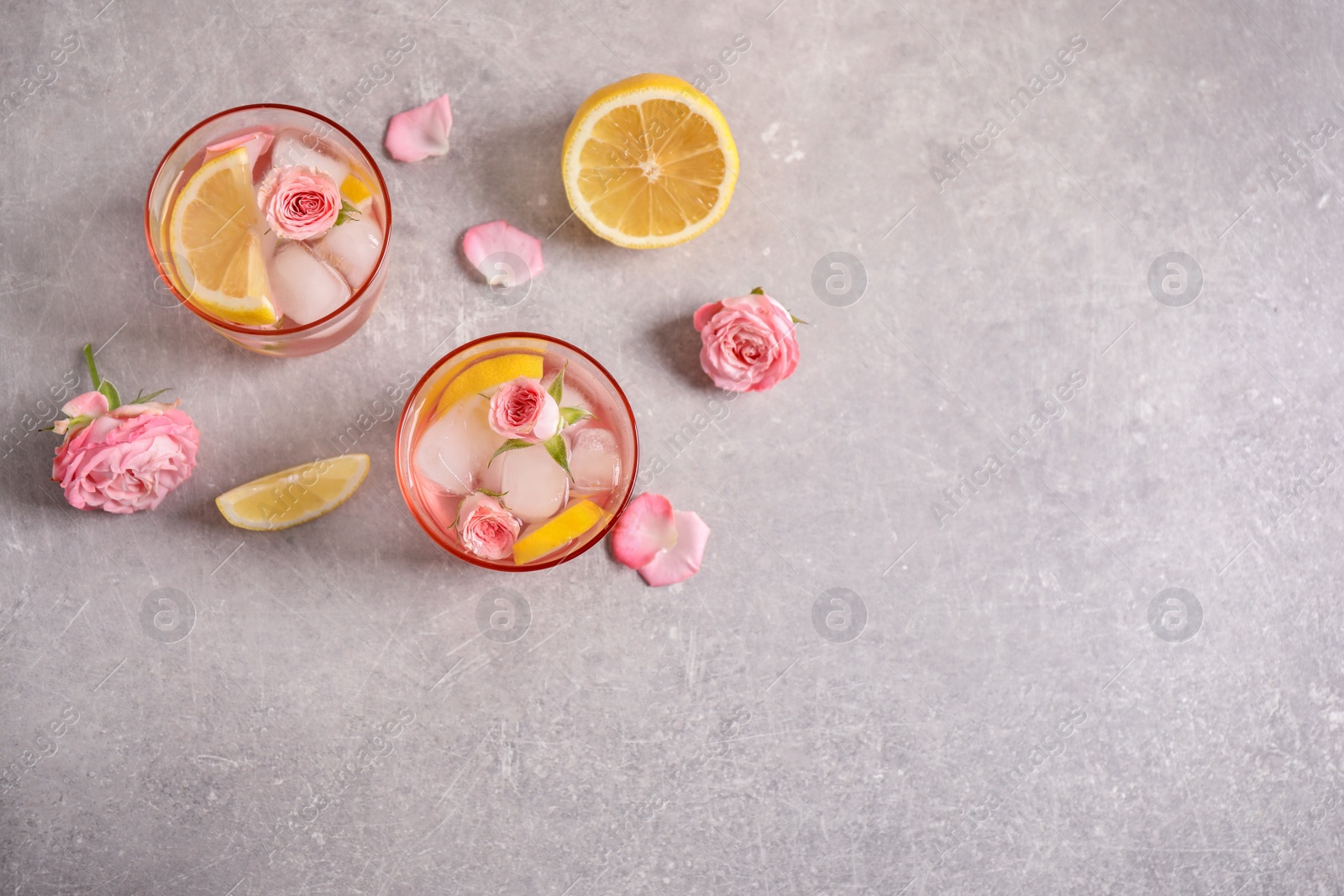 Photo of Tasty refreshing lemon drink with roses on light grey table, flat lay. Space for text