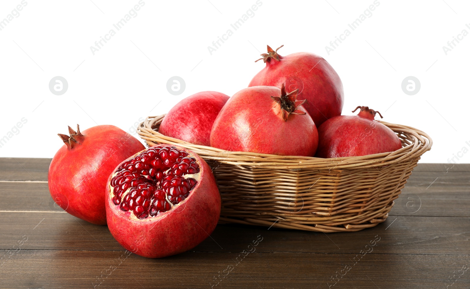 Photo of Fresh pomegranates in wicker basket on wooden table against white background