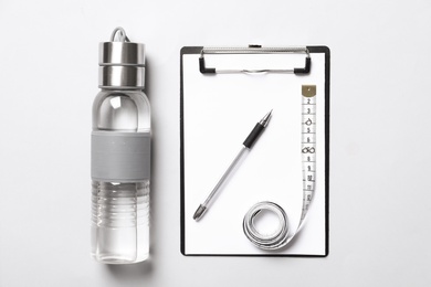 Photo of Bottle of water, near clipboard with pen and measuring tape on white background, flat lay