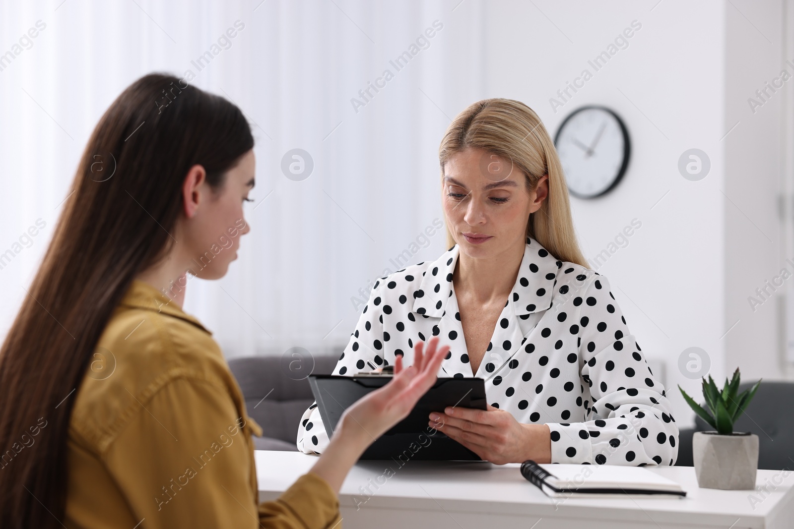 Photo of Psychologist holding clipboard while working with teenage girl at table in office