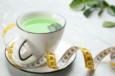 Photo of Cup of herbal diet tea and measuring tape on light table