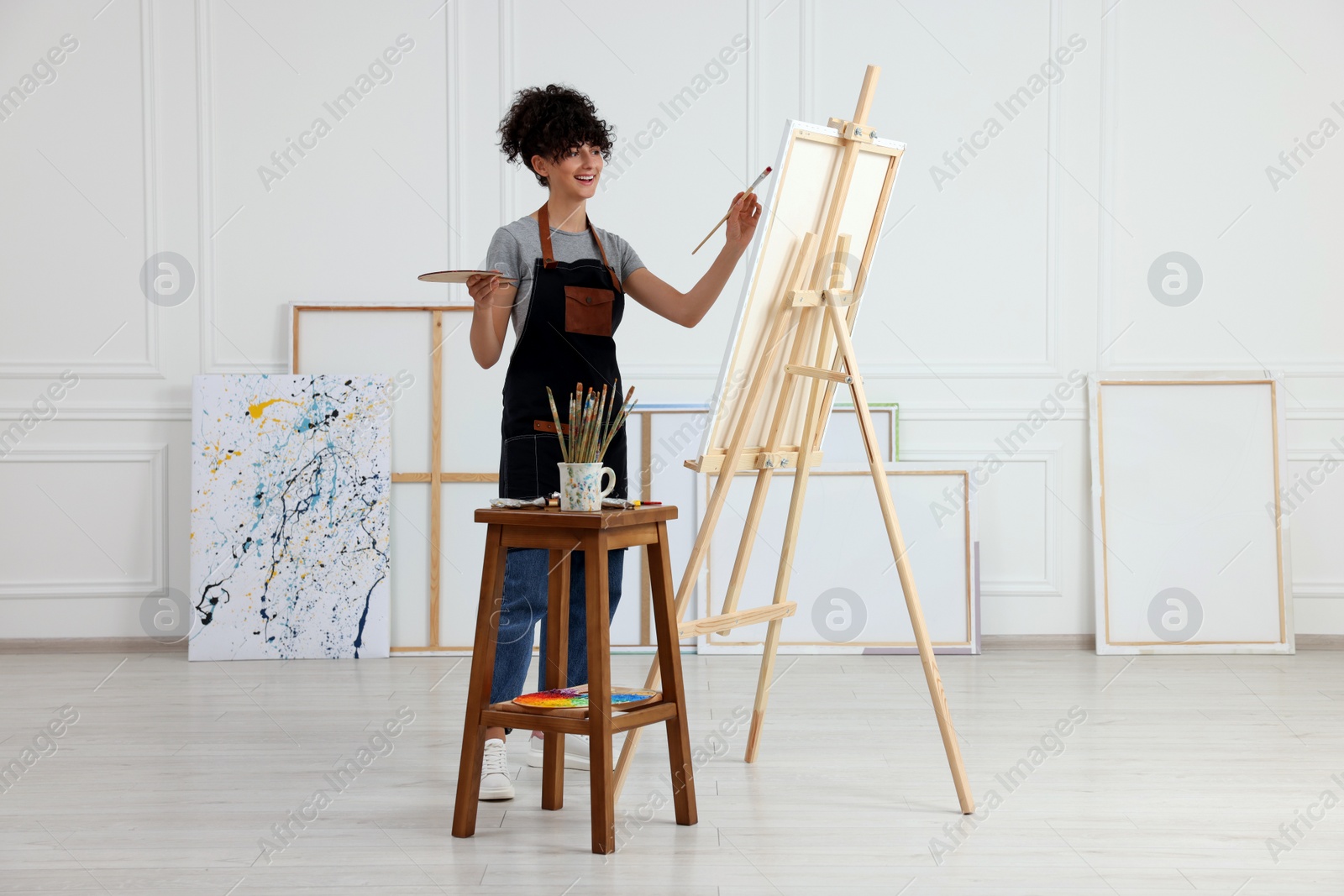 Photo of Young woman painting on easel with canvas in studio