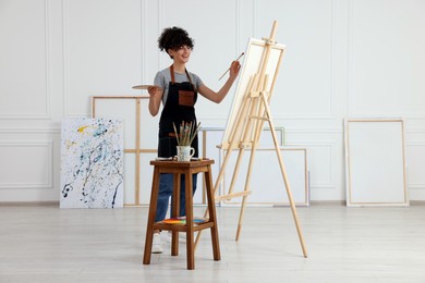 Photo of Young woman painting on easel with canvas in studio