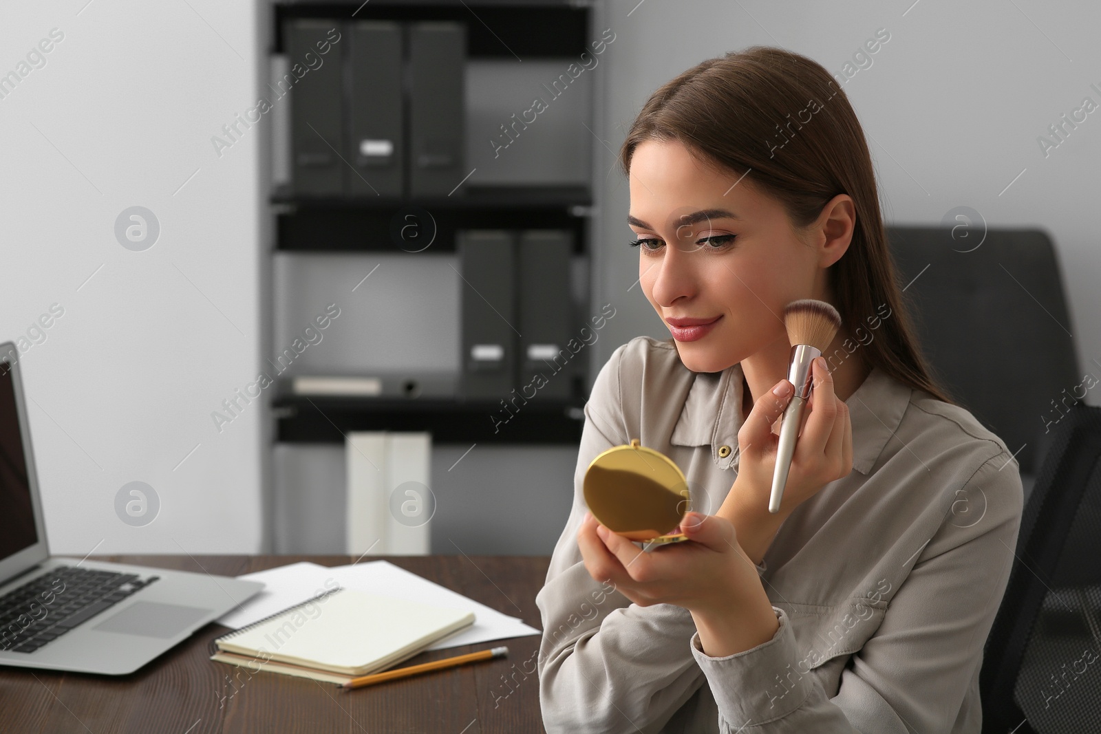 Photo of Young woman with cosmetic pocket mirror doing makeup at table indoors, space for text
