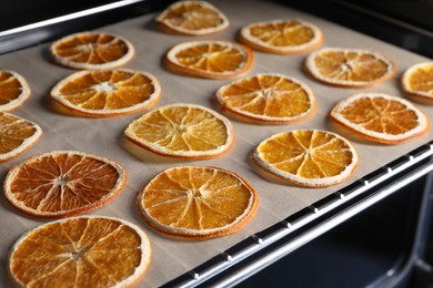 Photo of Many dry orange slices on parchment paper in oven, closeup