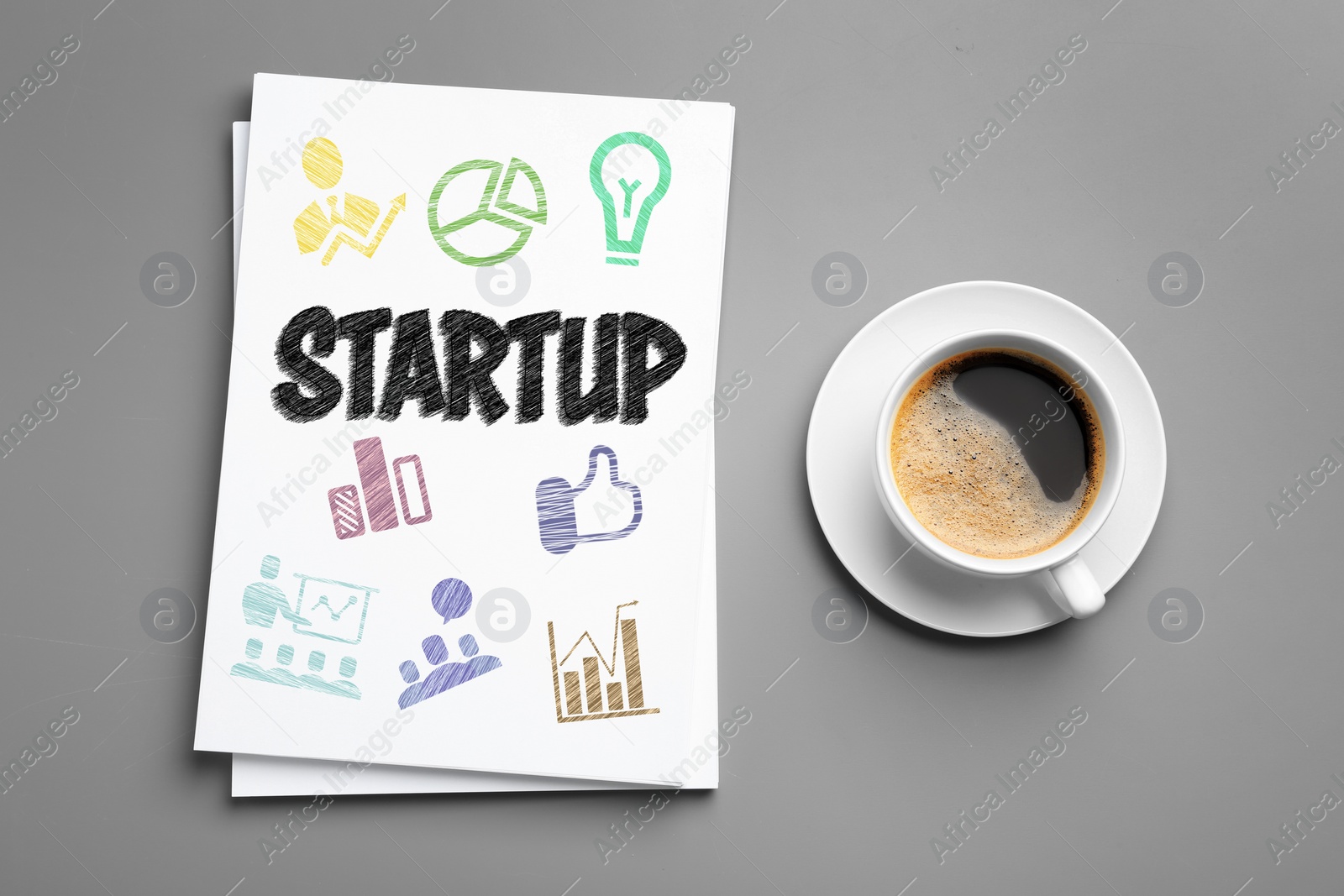 Image of Paper sheets with word STARTUP and drawn colorful icons near cup of coffee on grey background, flat lay