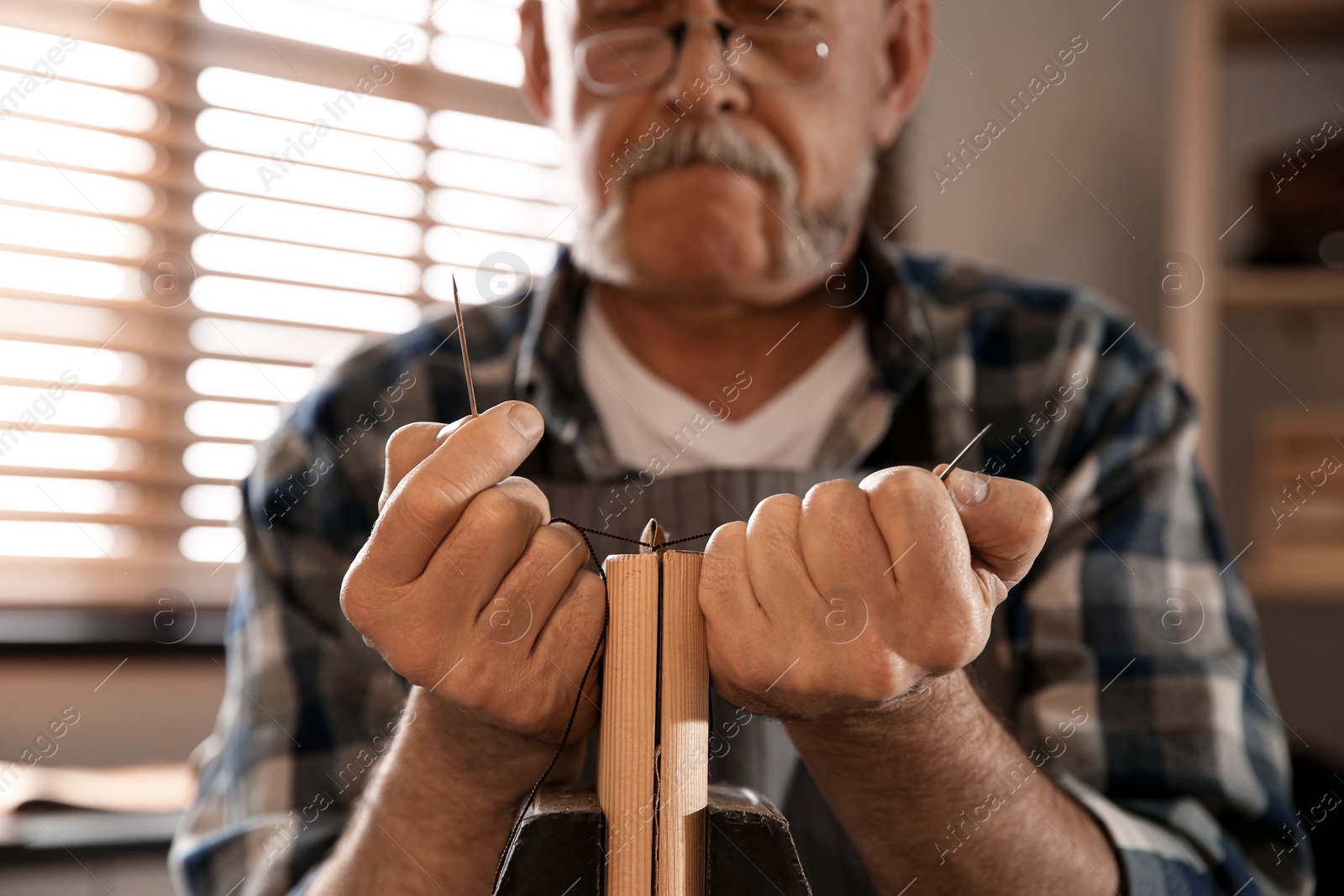 Photo of Man sewing piece of leather in workshop, closeup