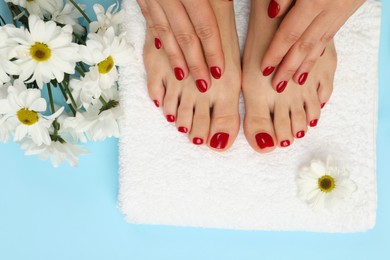 Photo of Woman with stylish red toenails after pedicure procedure and chamomile flowers on light blue background, top view