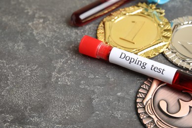 Photo of Medals and tube of blood with words Doping test on grey stone table. Space for text